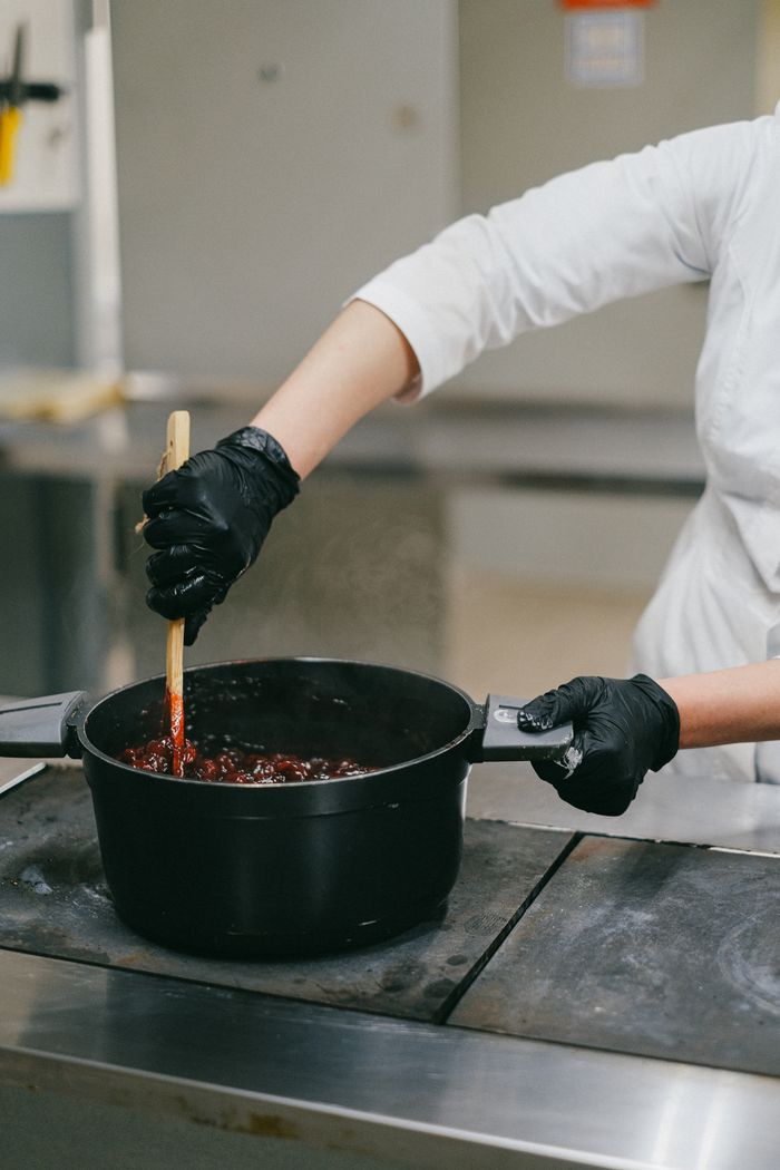 A chef stirs a dish in a black pot, highlighting culinary preparation in a professional kitchen.